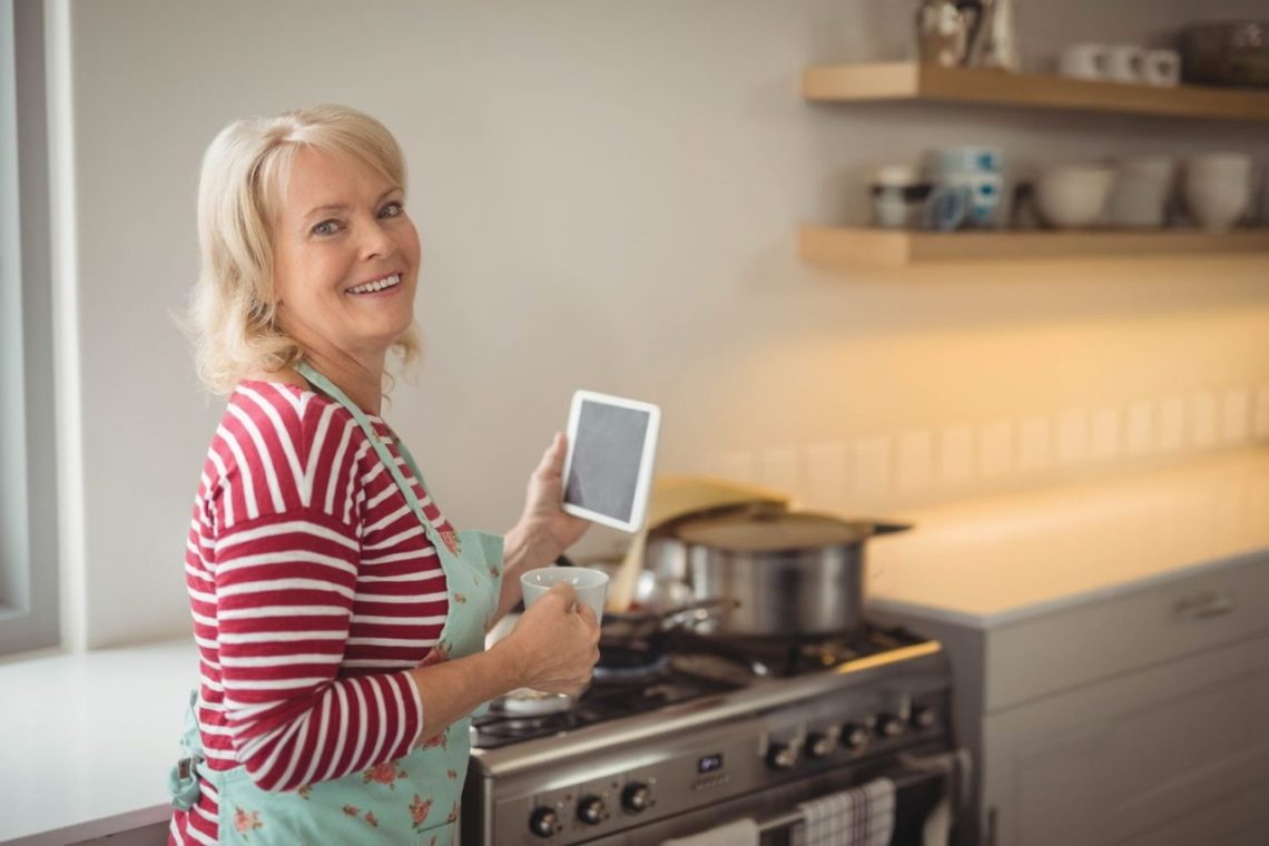 Une femme âgée dans sa cuisine vérifie la cuisinière à gaz avec attention.