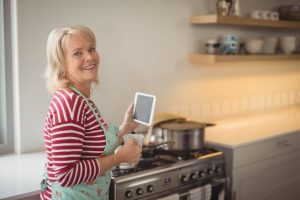 Une femme âgée dans sa cuisine vérifie la cuisinière à gaz avec attention.