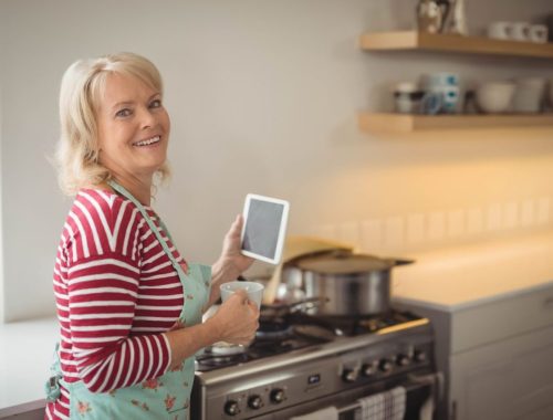 Une femme âgée dans sa cuisine vérifie la cuisinière à gaz avec attention.