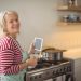 Une femme âgée dans sa cuisine vérifie la cuisinière à gaz avec attention.
