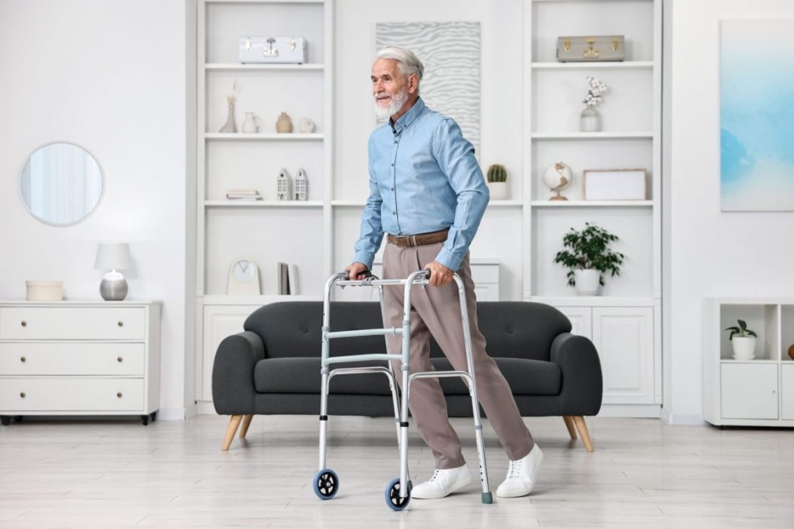 Senior utilisant un déambulateur dans un espace dégagé de son domicile pour faire des exercices de kinésithérapie en toute sécurité.