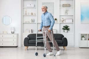 Senior utilisant un déambulateur dans un espace dégagé de son domicile pour faire des exercices de kinésithérapie en toute sécurité.