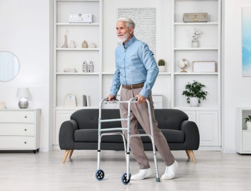 Senior utilisant un déambulateur dans un espace dégagé de son domicile pour faire des exercices de kinésithérapie en toute sécurité.