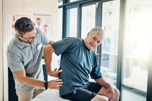 Un senior échange avec un ostéopathe au sujet d’une douleur lombaire, dans un cabinet de soins.