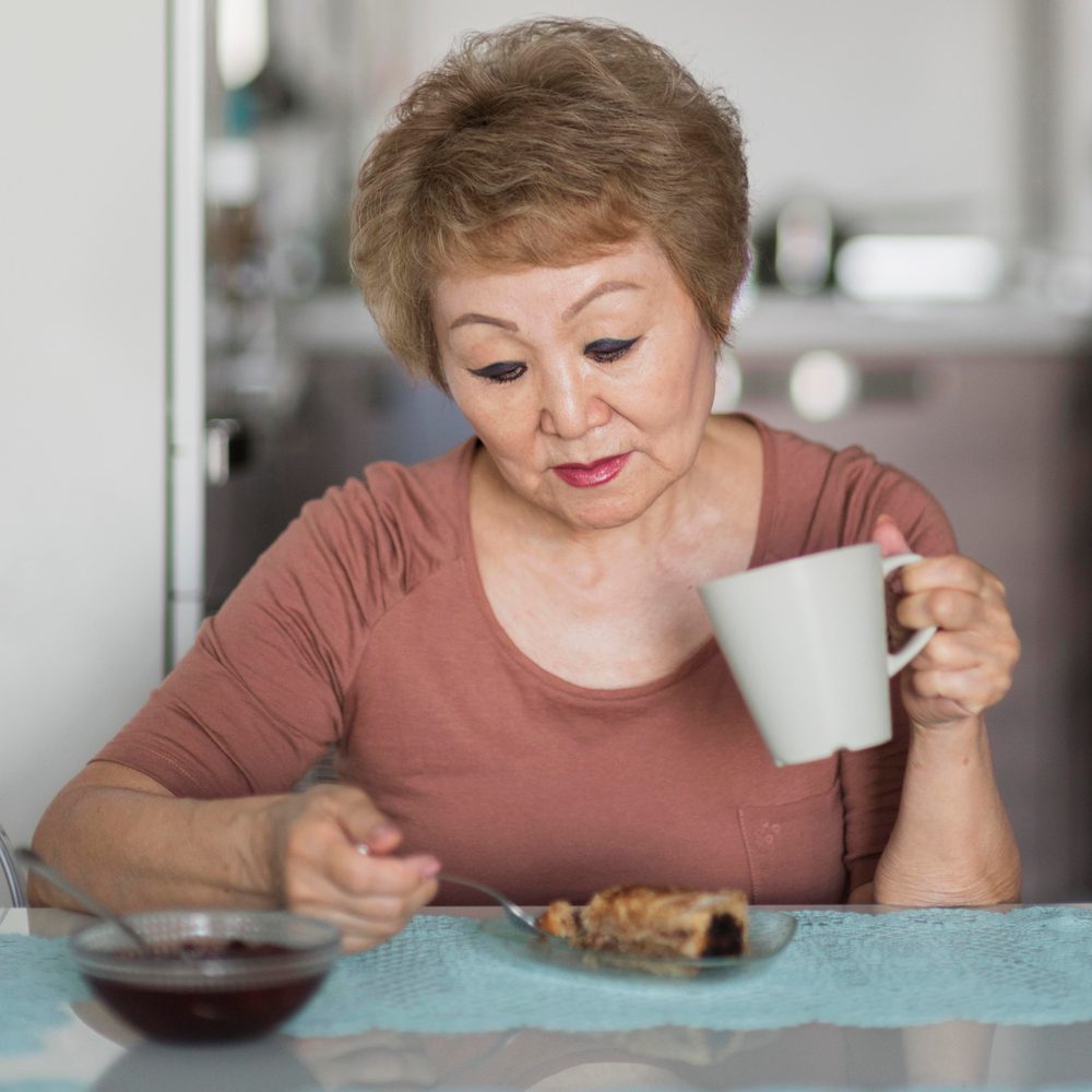 Une senior regarde son repas sans appétit dans sa cuisine.