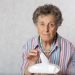 Femme âgée assise à table devant une assiette presque intacte après un veuvage.