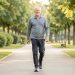 Un homme senior de plus de 60 ans marche calmement sur un chemin plat avec des chaussures de sport adaptées, dans un environnement naturel baigné de lumière douce.