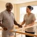 Un homme martiniquais de plus de 60 ans réalise des exercices d’équilibre encadrés par un professionnel dans une salle lumineuse et rassurante.
