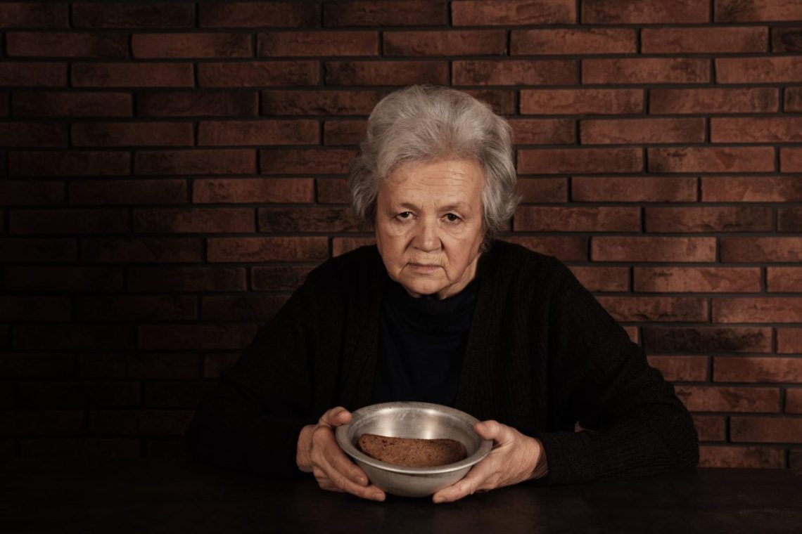 Une personne âgée assise à table devant une assiette presque intacte, avec un air fatigué.