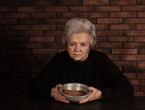 Une personne âgée assise à table devant une assiette presque intacte, avec un air fatigué.