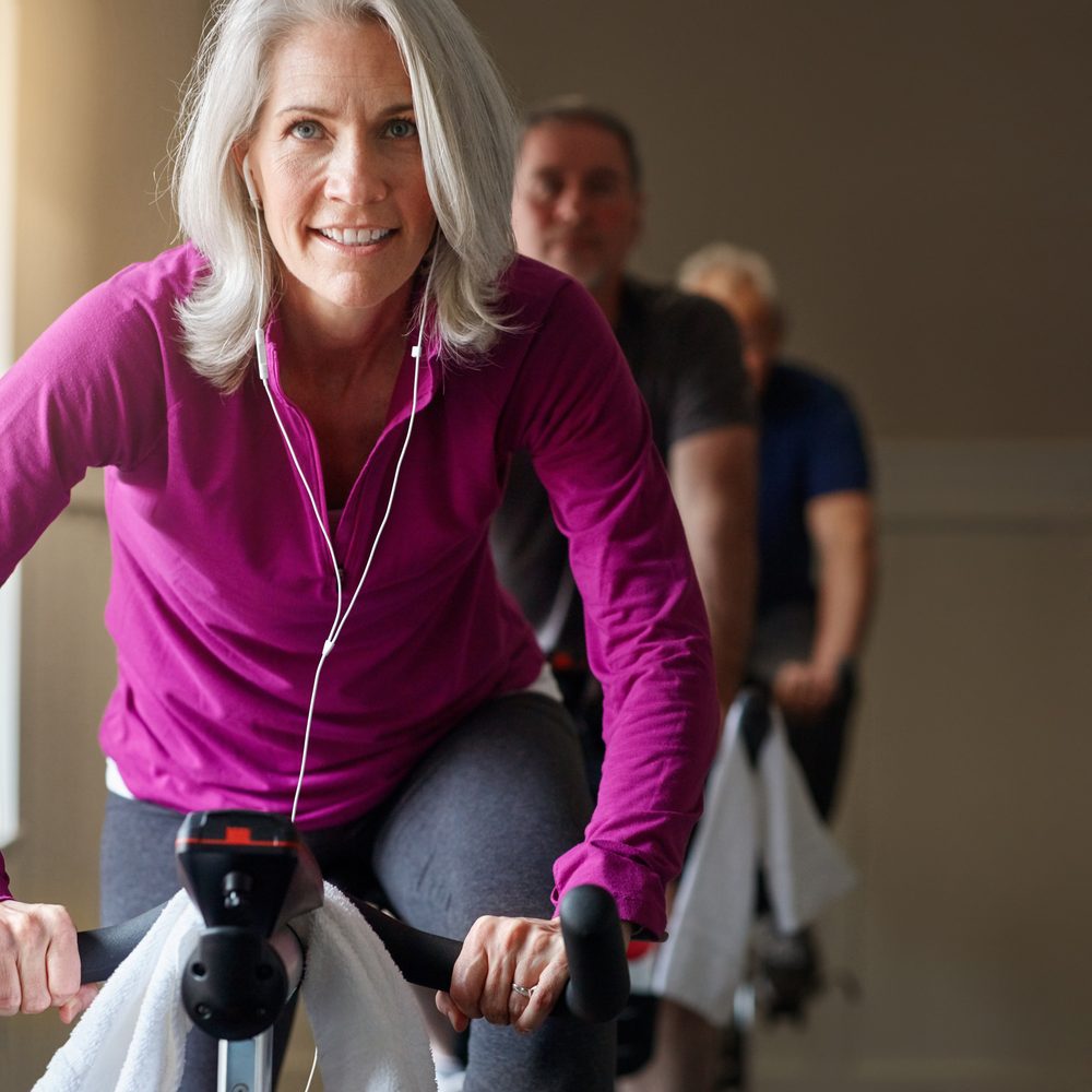 Une sportive âgée s’exerce sur un vélo stationnaire, dans le cadre d’une reprise progressive et encadrée.