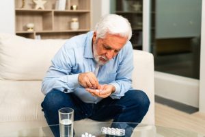 Un senior prend ses médicaments avec un verre d’eau, accompagné avec attention par un proche.