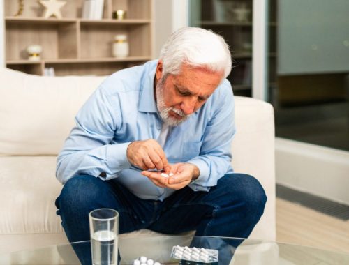 Un senior prend ses médicaments avec un verre d’eau, accompagné avec attention par un proche.