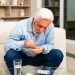 Un senior prend ses médicaments avec un verre d’eau, accompagné avec attention par un proche.
