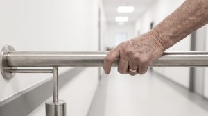 Une personne âgée marche prudemment dans un couloir dégagé équipé d’une rampe murale.