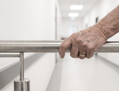 Une personne âgée marche prudemment dans un couloir dégagé équipé d’une rampe murale.