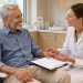 Un homme senior souriant échange avec une dentiste dans un cabinet lumineux au sujet d’une prothèse dentaire complète.
