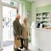 Un homme âgé accompagné de sa fille est accueilli par une professionnelle de santé à l’entrée d’une pharmacie française.